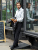 Man standing on a step with a phone and jacket, reflected in a store window, wearing refined clothing from the Stain Defender collection.